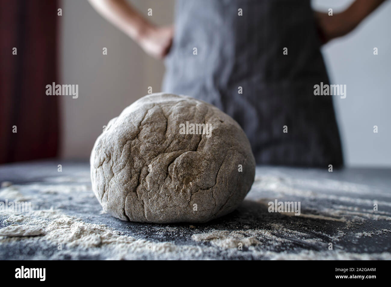 Baker is in a pose with hands on hips, pleased and proud that does its job and knead the dough on a black table Stock Photo