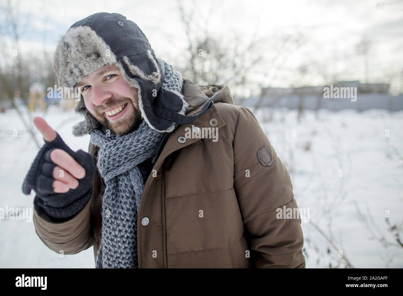 smiling man shows and explains the index finger in the winter outdoors in a fur hat and jacket Stock Photo