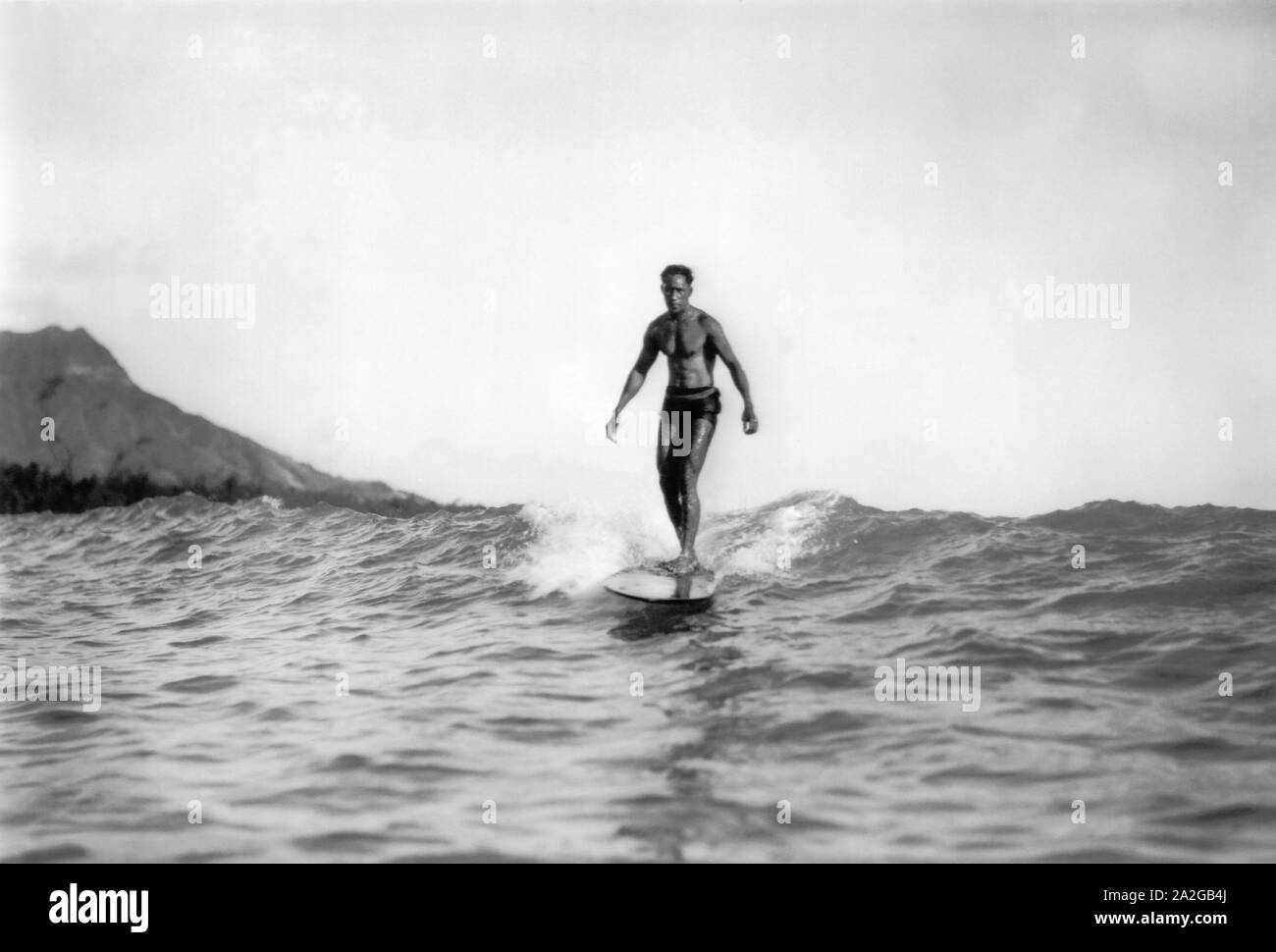 Olympic Gold Medal swimmer and Father of Modern Surfing, Duke Kahanamoku, riding a wave on a wooden surfboard in Waikiki, Hawaii with Diamond Head in the background. Stock Photo