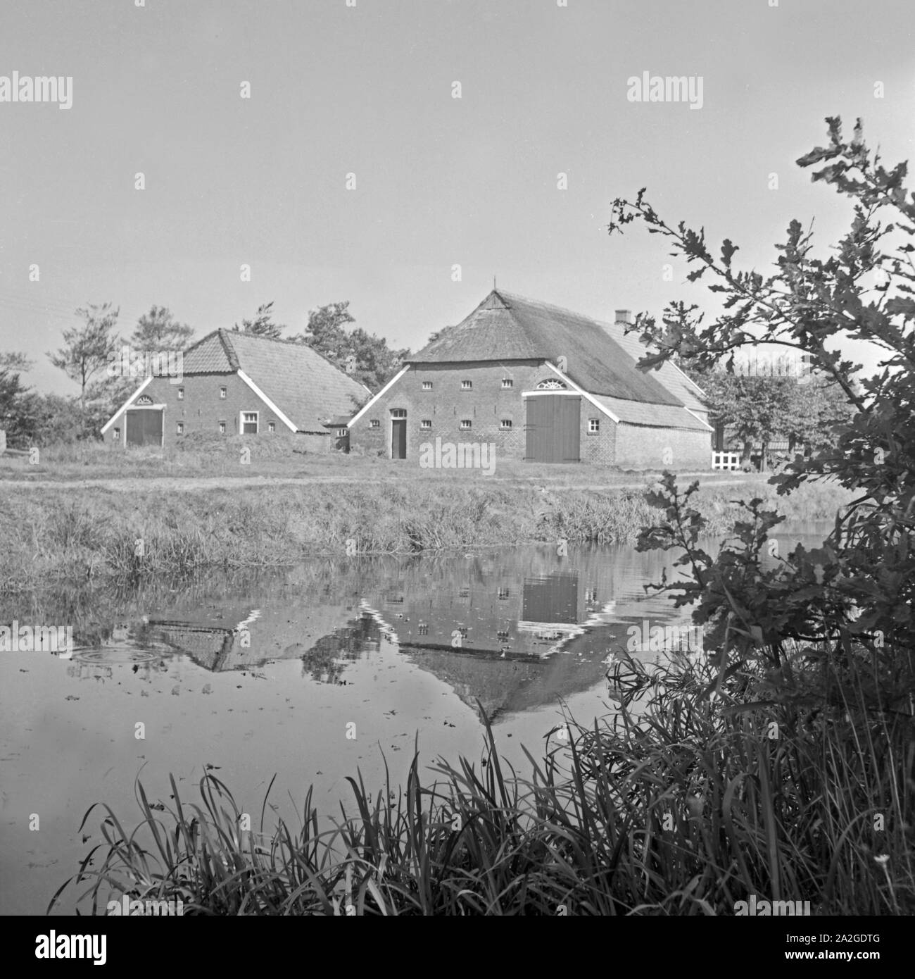 Im Wasser spiegelnde rote Häuser in Ostfriesland, Deutschland 1930er Jahre. Red brick houses reflecting in the moor water in East Frisia, Germany 1930s. Stock Photo