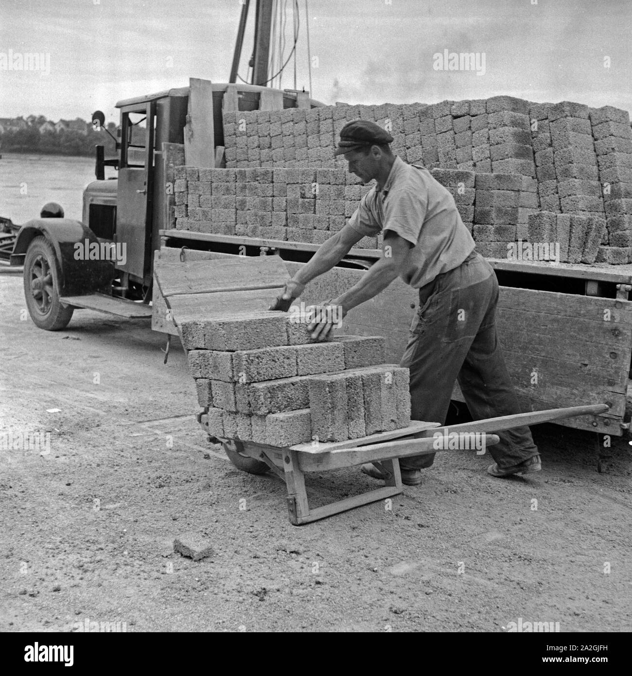 Ein Arbeiter verlädt Schlemmsteine vom LKW auf eine Schubkarre, Deutschland 1930er Jahre. Worker loading Rhenish bricks from a truck to a barrow, Germany 1930s. Stock Photo
