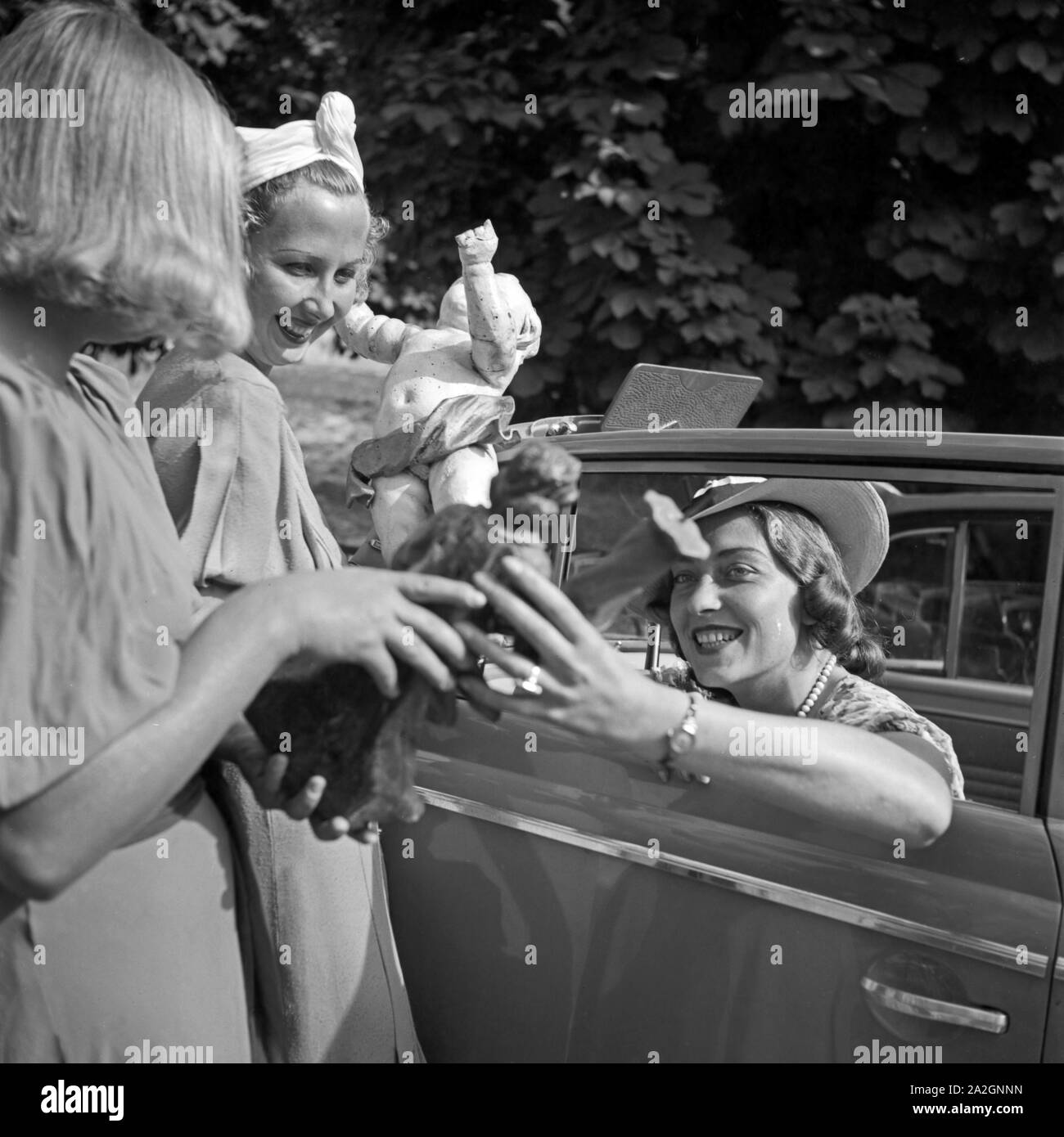 Drei Frauen unterhalten sich aus dem Auto heraus über den Kauf von Kunsthandwerk, Deutschland 1930er Jahre. Three women chatting out from a convertible about a purchase of craftwork, Germany 1930s. Stock Photo