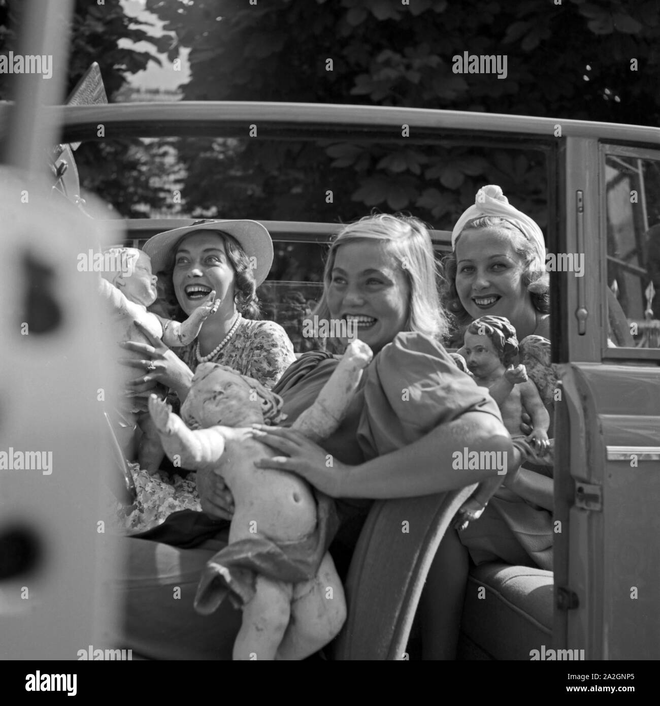 Drei junge Frauen mit einer Putte im offenen Wagen, Deutschland 1930er Jahre. Three young women playing with a putto in an open car, Germany 1930s. Stock Photo