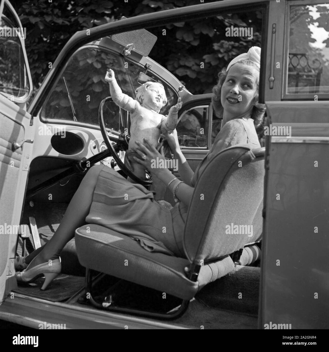 Eine junge Frau mit einer Putte im offenen Wagen, Deutschland 1930er Jahre. A young woman playing with a putto in an open car, Germany 1930s. Stock Photo