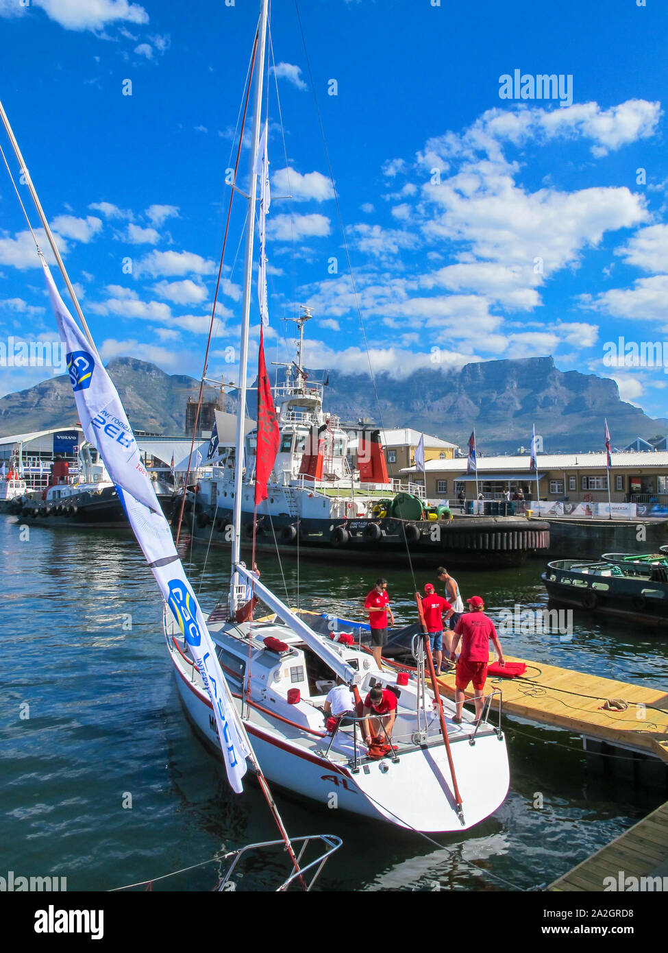 yacht moored in Table Bay harbour with people wearing red clothing and in the background Table Mountain, Cape Town, South Africa Stock Photo