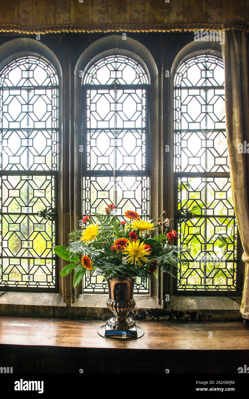 Hever Castle clear sectioned art glass, curtained, three arched panels of window panes, colorful flower arrangement on wooden table. Stock Photo