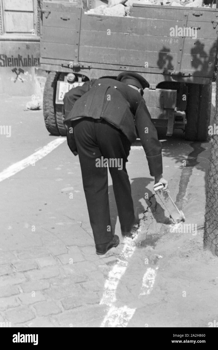 Ein Polizist streut Kalk auf eine Benzinspur bei einem Verkehrsunfall, Deutschland 1930er Jahre. A policeman strewing chalk to a petrol track at a traffic accident, Germany 1930s. Stock Photo