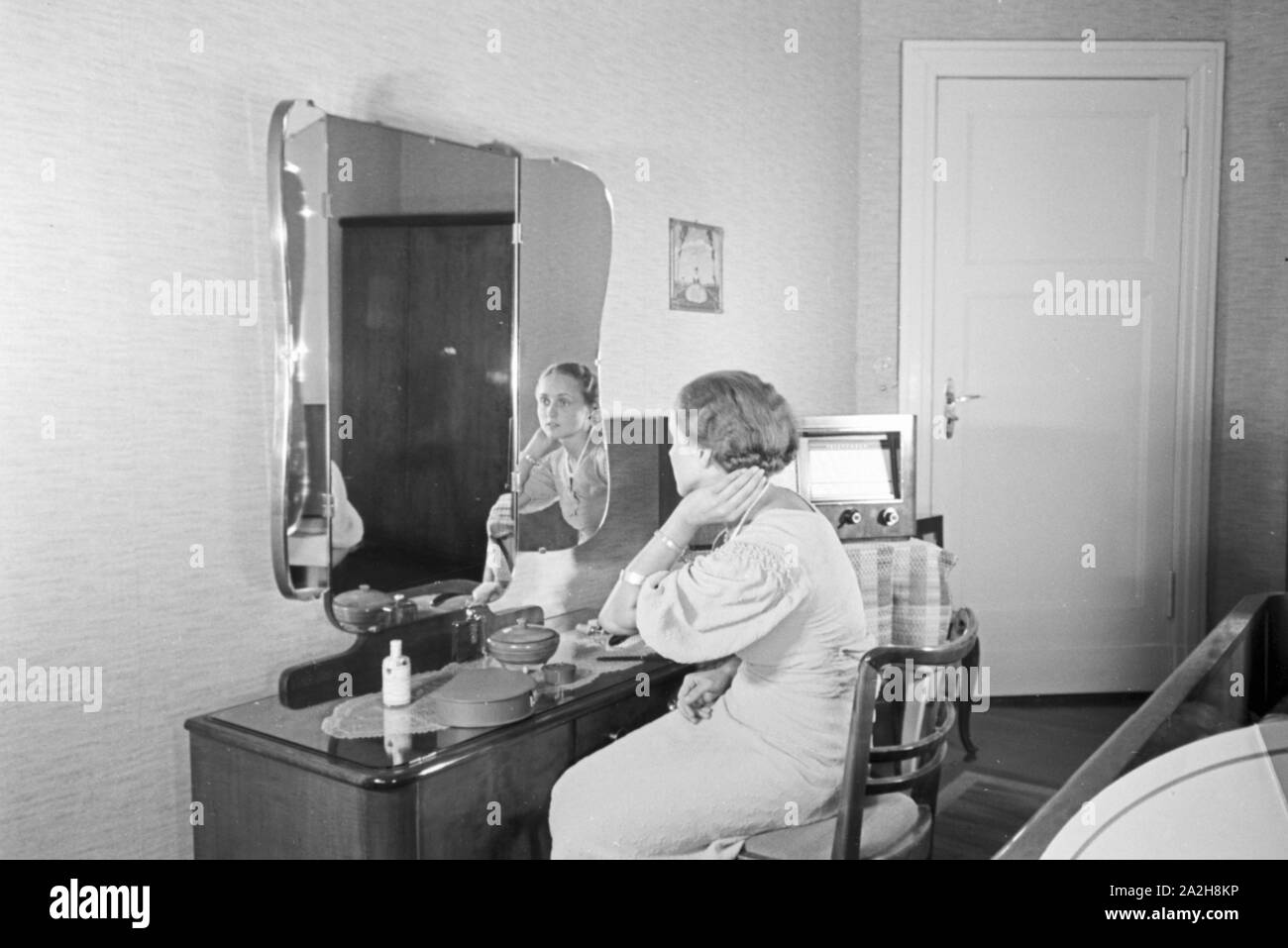 Eine Frau sitzt am Frisiertisch und hört Radio, Deutschland 1930er Jahre. A woman sitting at the dressing table while listening to the radio, Germany 1930s. Stock Photo