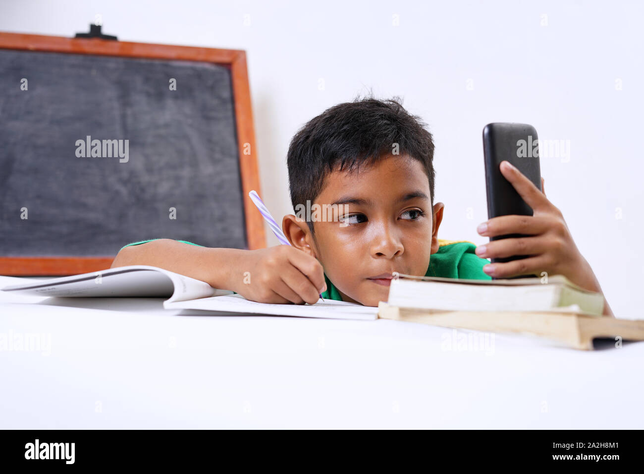 Boy playing with smartphone while doing homework Stock Photo