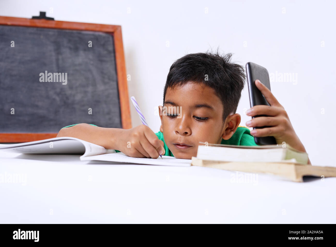 Boy playing with smartphone while doing homework Stock Photo
