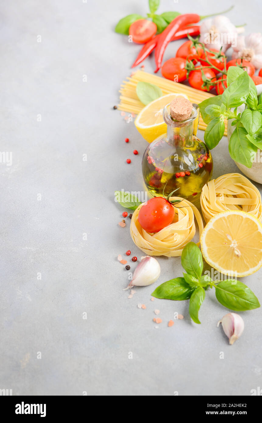 Italian food ingredients – pasta, tomatoes, basil and olive oil on gray concrete background. Stock Photo