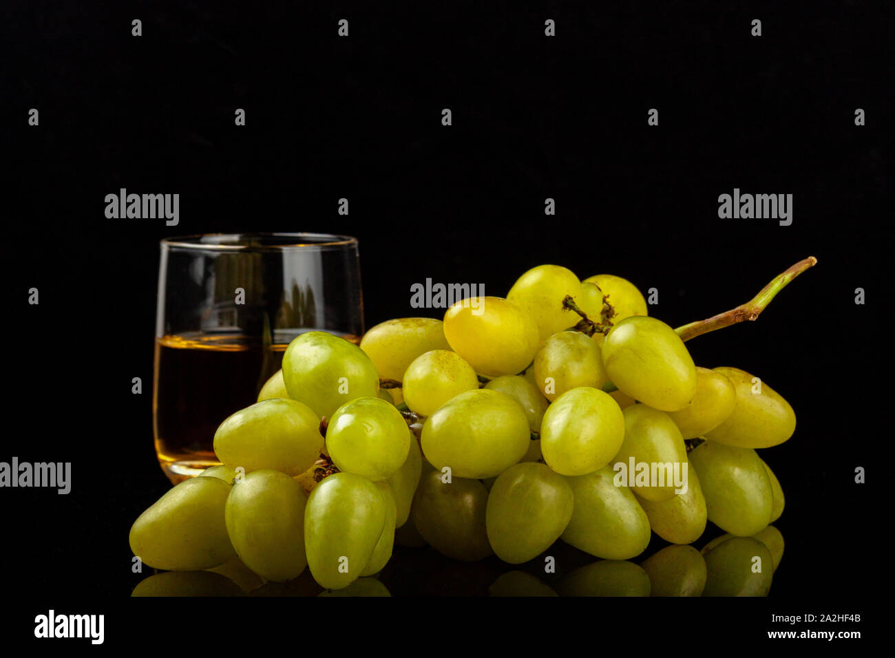 Two glasses of white wine and a bunch of grapes isolated on black Stock Photo