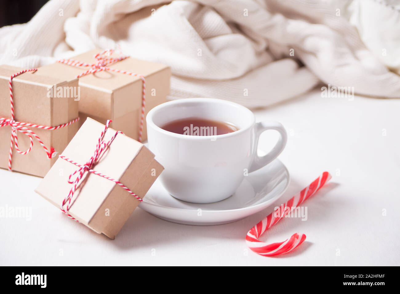 Cup of tea, candy cane, Christmas gift boxes, knitted plaid on the white background. Stock Photo