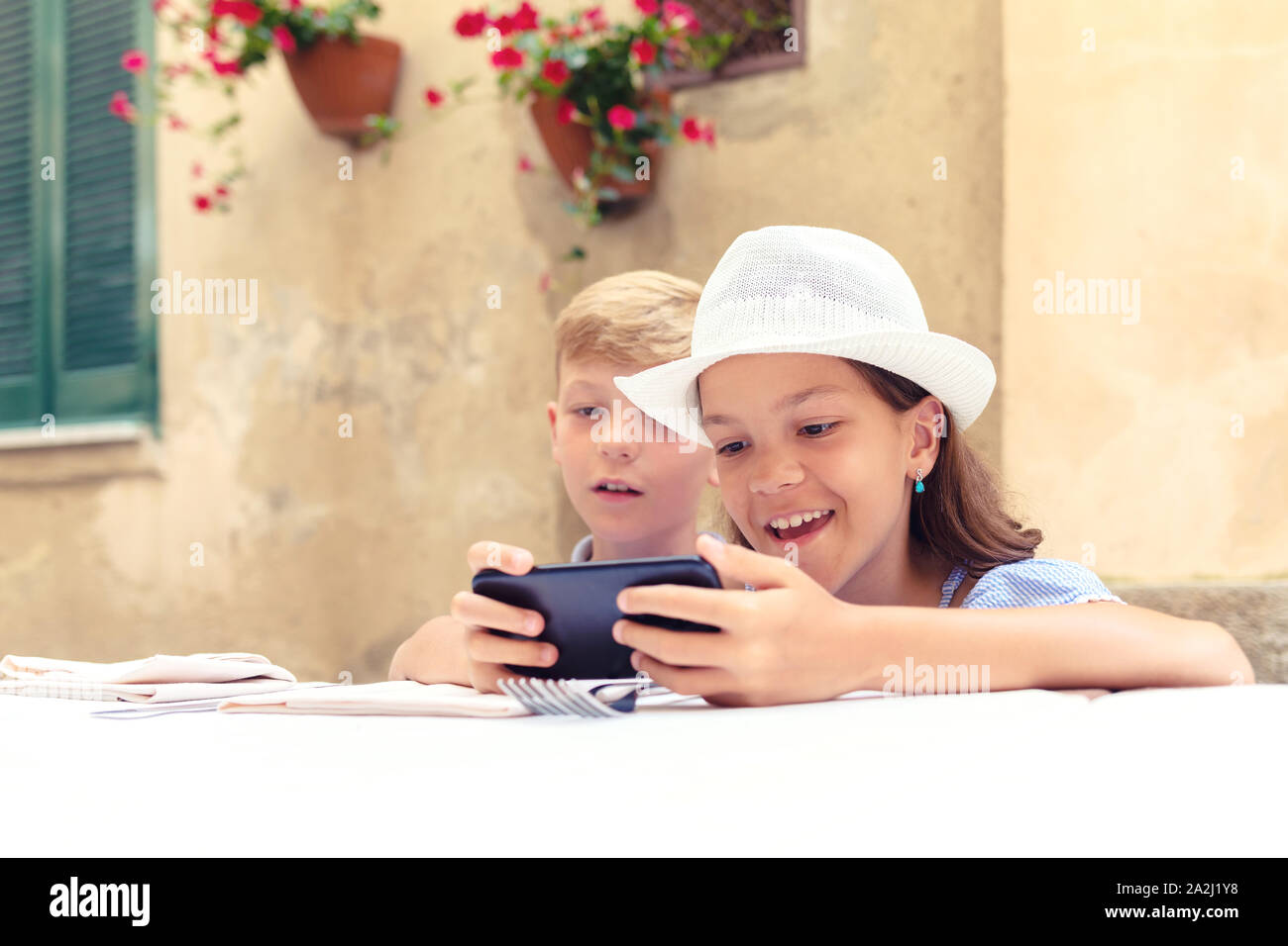 Happy kids playing with mom’s smartphone waiting for food at restaurant – boy and girl spending time in front of screen phone - children addiction Stock Photo