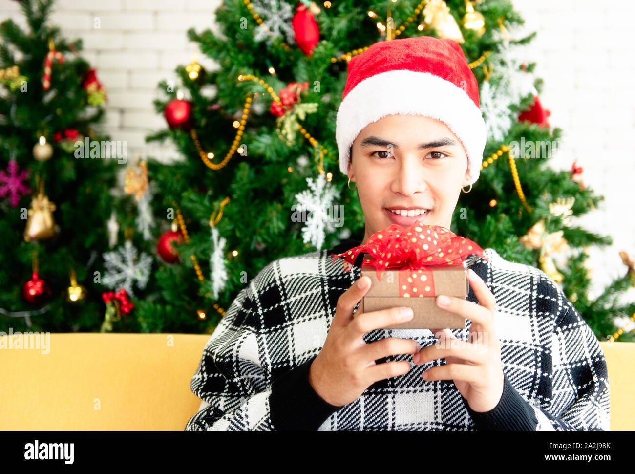 A young man wearing a Santa with a Christmas tree on the back. He smiled and was happy to get a box Christmas gift from his girlfriend. Close up and c Stock Photo
