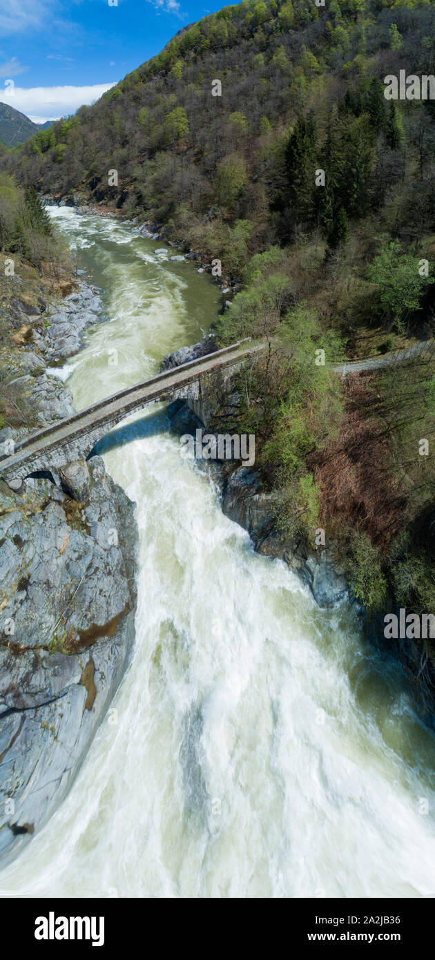 Alpine river in spring, large water flow for melting glaciers. Aerial view on the water current and on an ancient stone bridge. Sesia river in Piedmon Stock Photo
