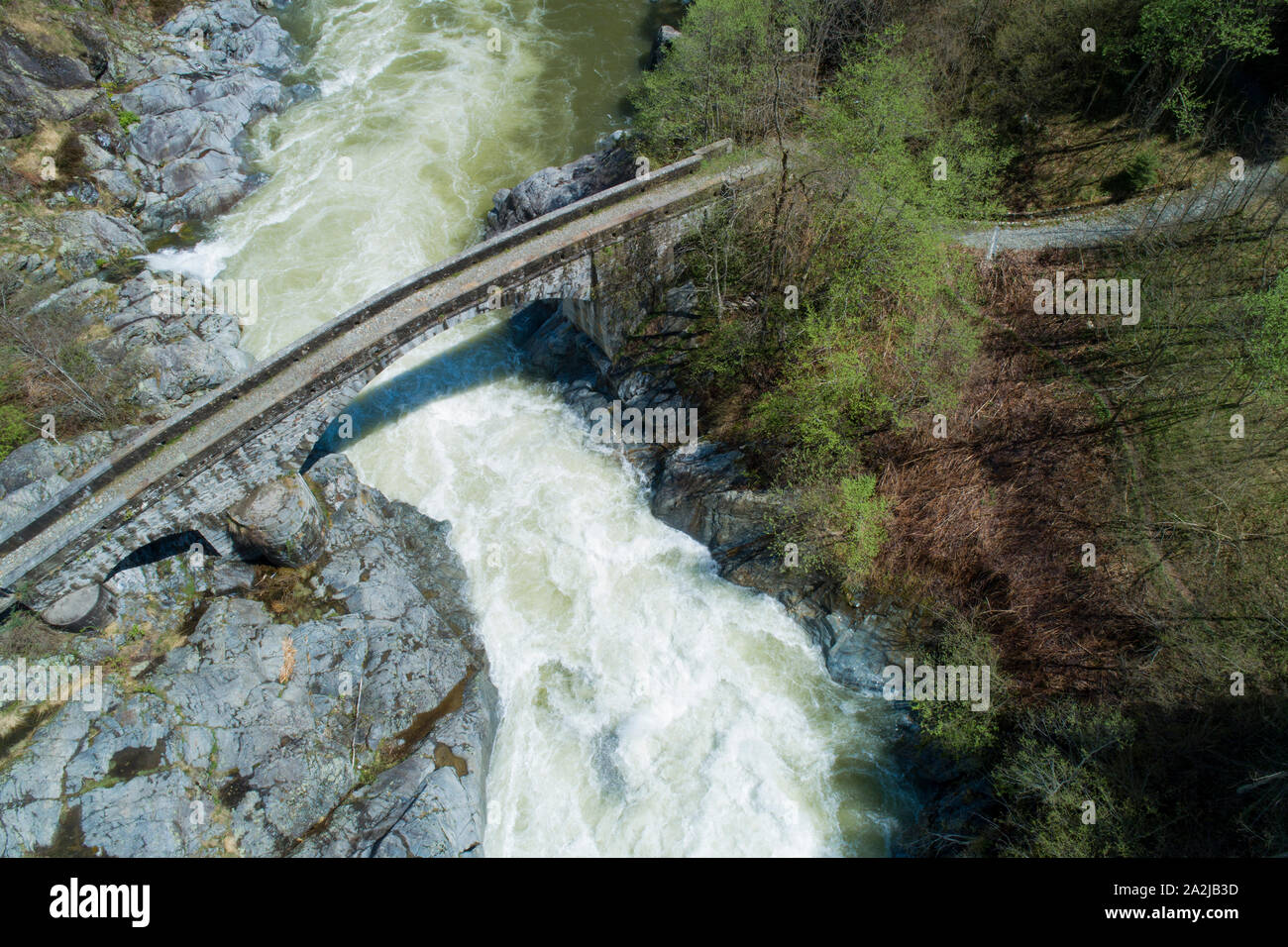 Alpine river in spring, large water flow for melting glaciers. Aerial view on the water current and on an ancient stone bridge. Sesia river in Piedmon Stock Photo