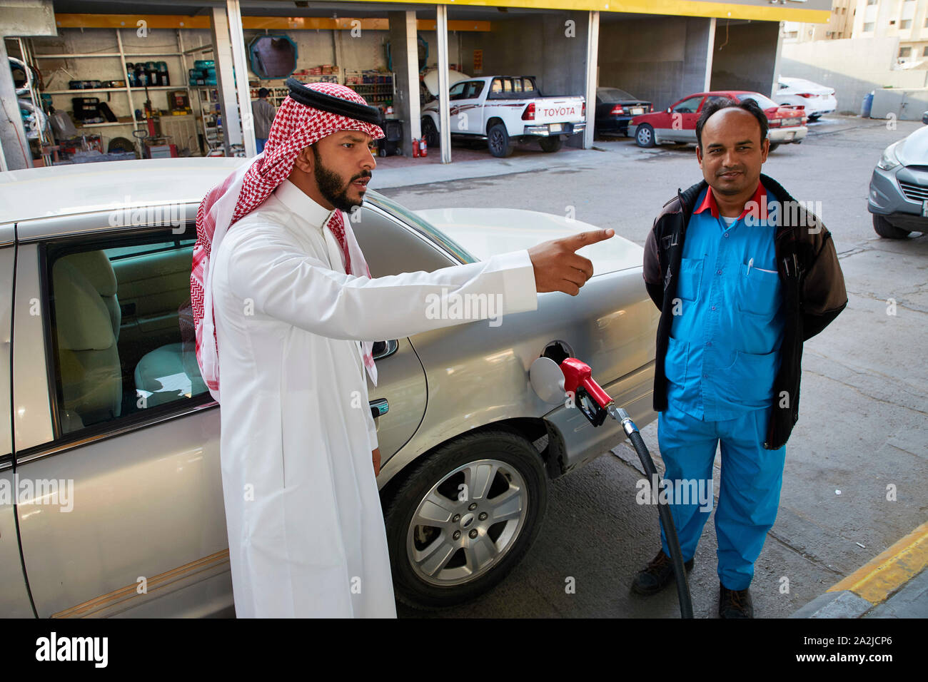 Saudia Arabia Saoedi Arabie Riyad Riaad Petrol for the car. A workingmigrant is helping a local Saudi man in traditional dress called a thobe or thawb Stock Photo