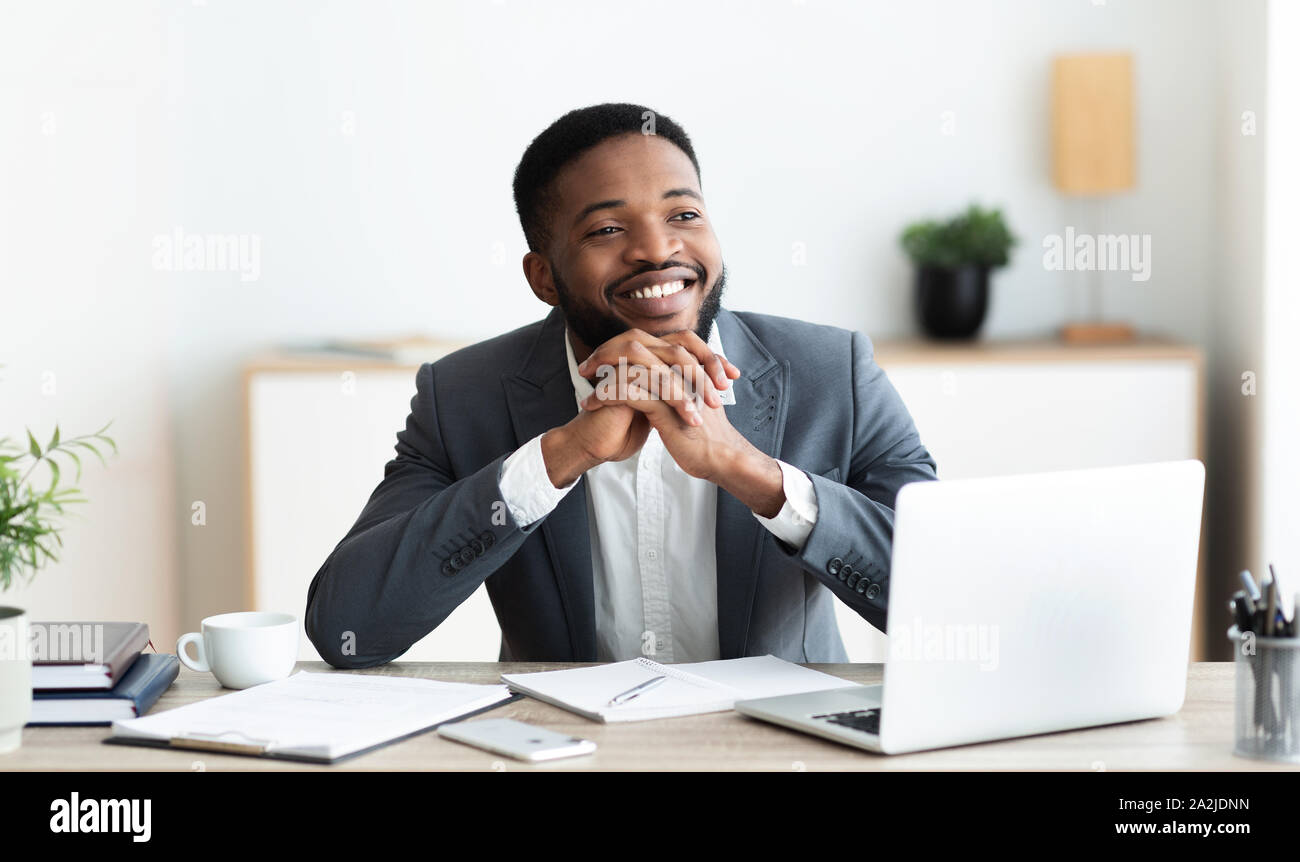 Pensive african businessman dreaming about something while working in office Stock Photo