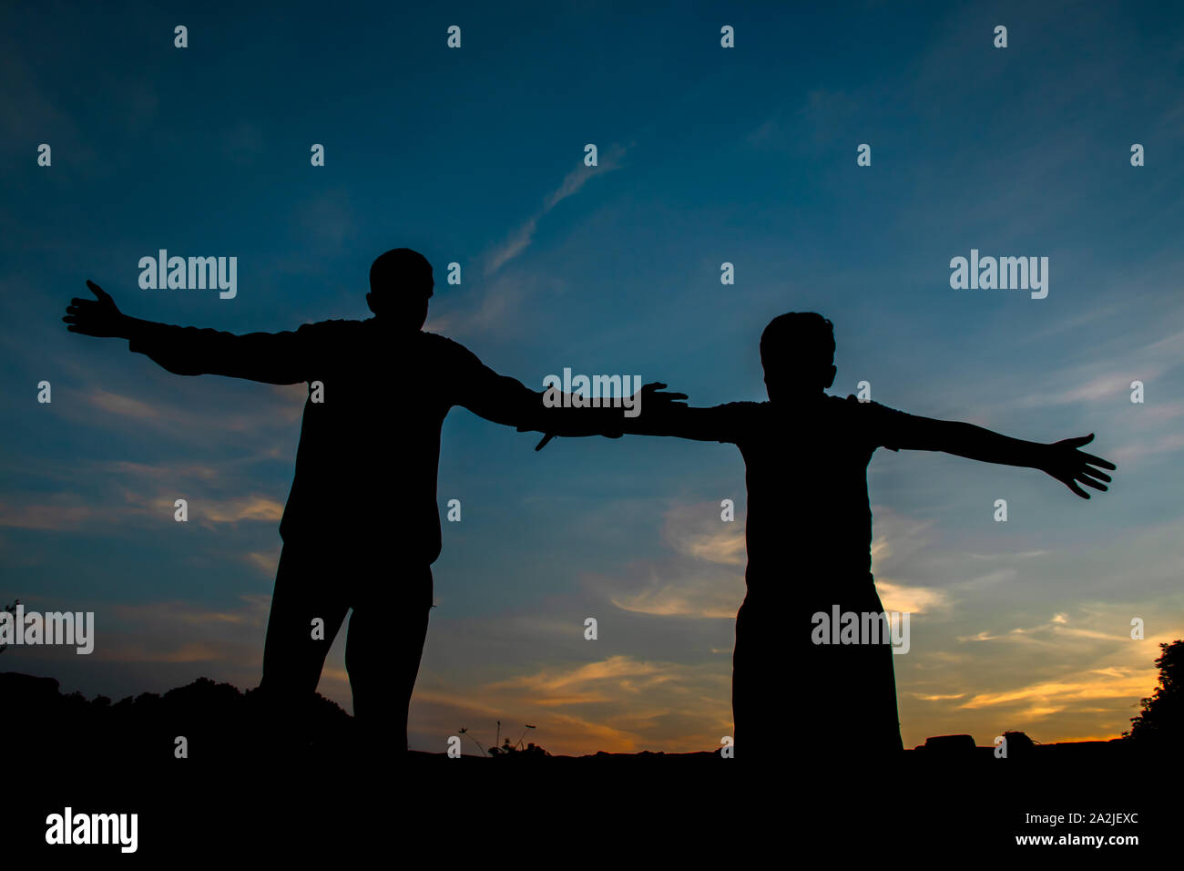 boys silhouette, over sunset sky, dark black shadow of male body with hands up, teenage boys having fun outdoor Stock Photo