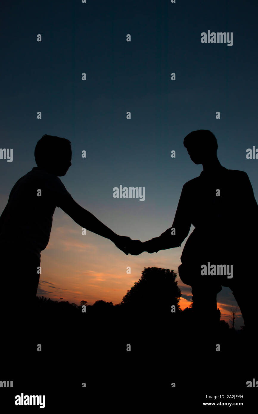 Silhouette, boys, are shaking each other hands in the colorful evening. Stock Photo