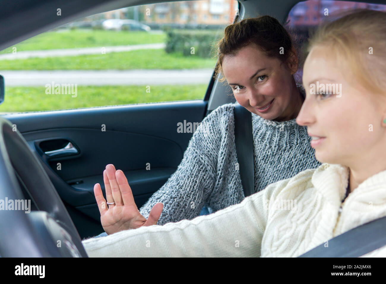 female instructor waves a friendly hand during a driving lesson with a female student Stock Photo