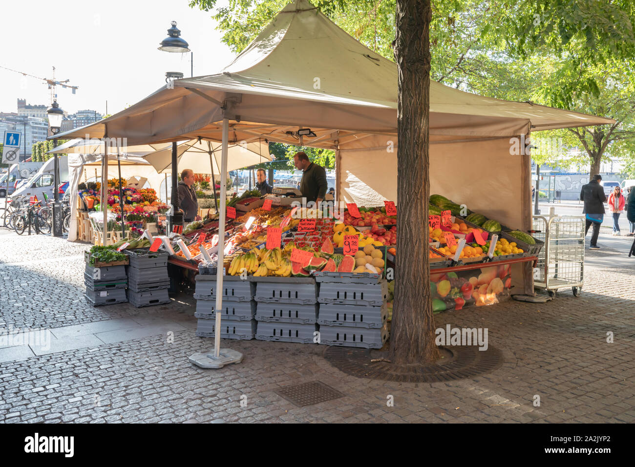 Stockholm, Sweden: A fruit stall with a white awning has produce stacked on  crates. All are sheltered beneath a tree. Three men converse Stock Photo -  Alamy