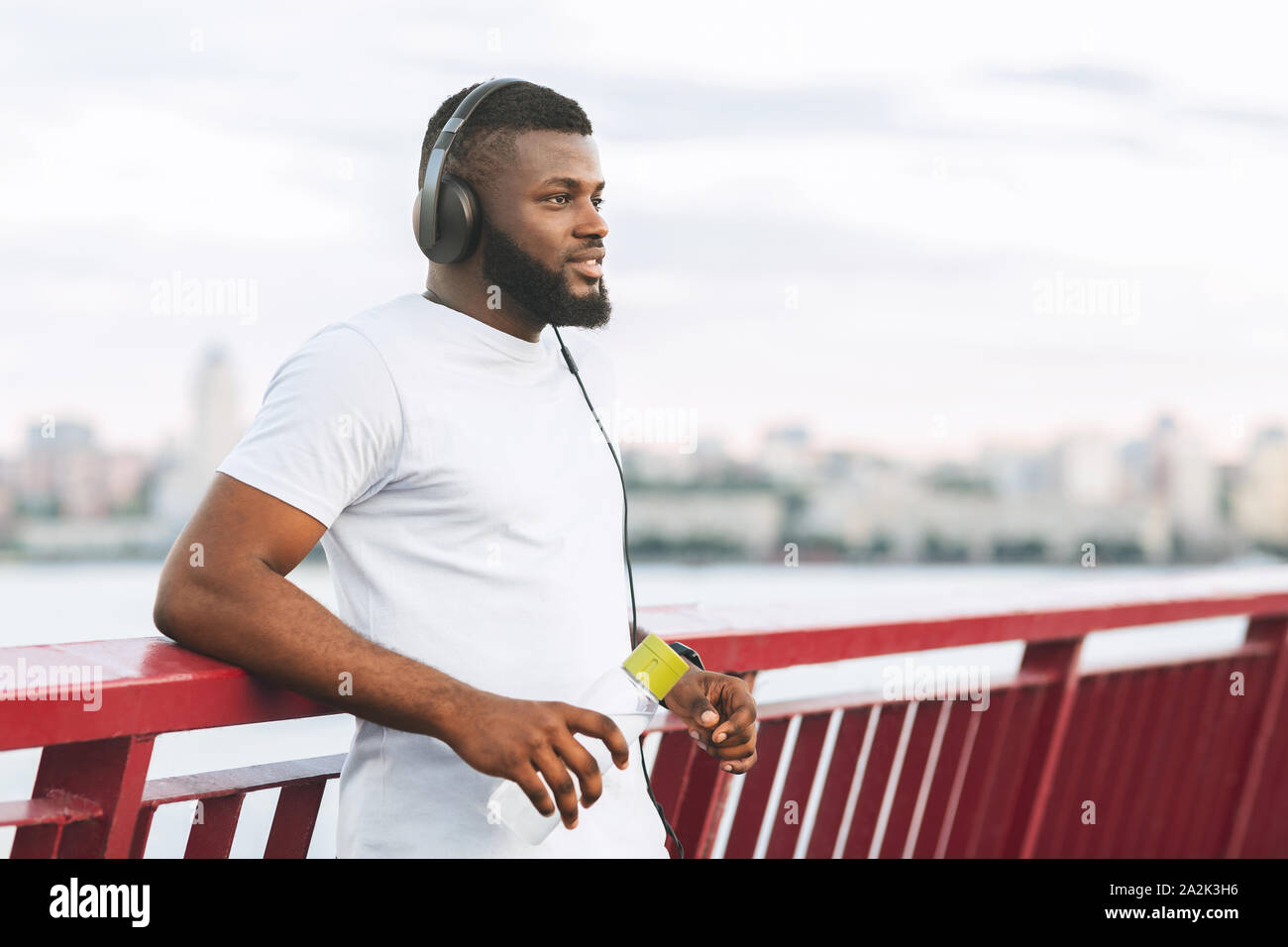 Dreamy black athletic guy resting on city bridge Stock Photo