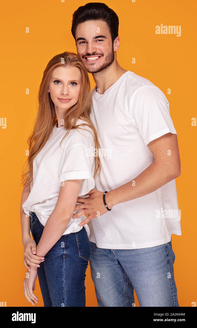 Happy beautiful couple wearing jeans and white shirts, posing in studio on  yellow background Stock Photo - Alamy