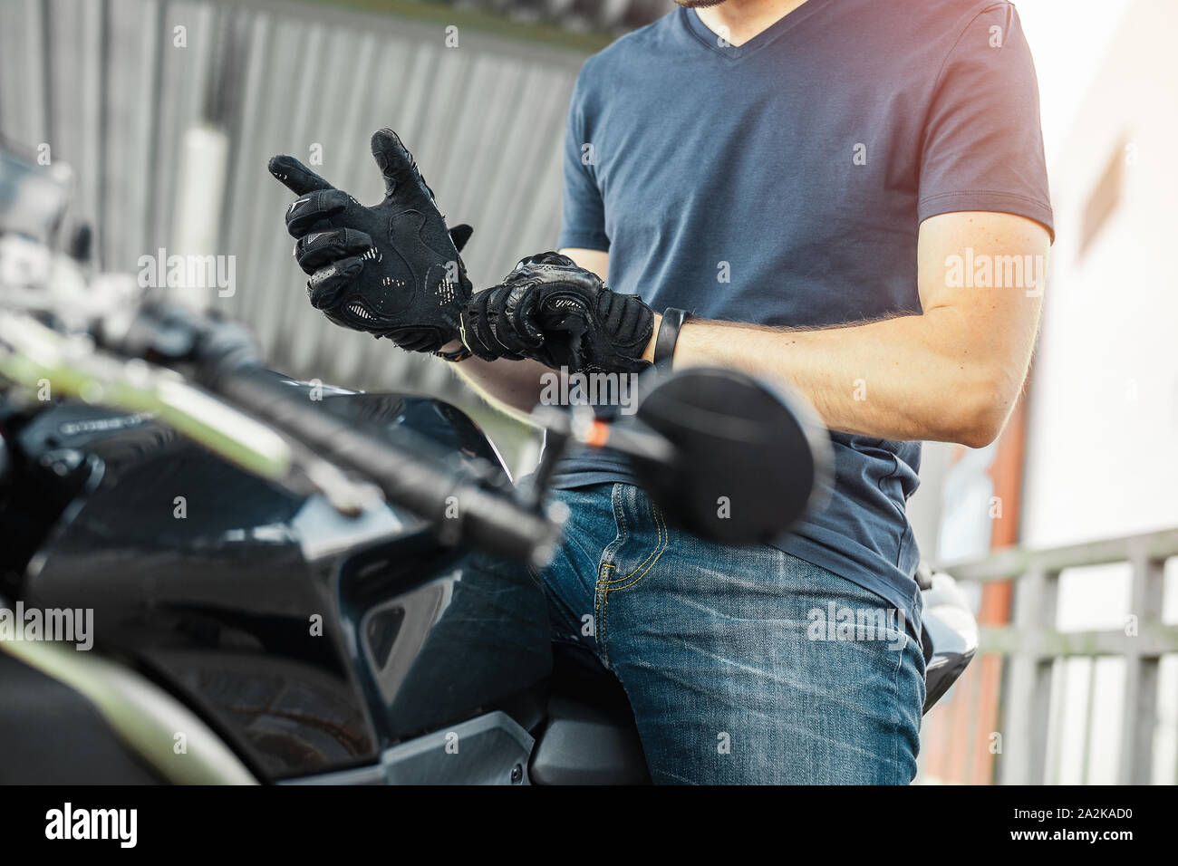 Close up of biker putting on black gloves and sitting on motorcycle