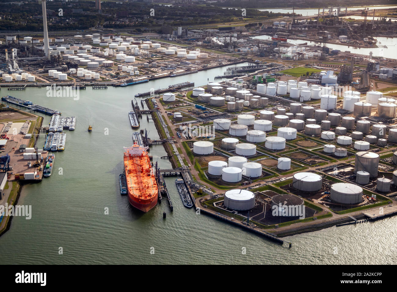 Aerial view of a large orange oil tanker moored at an oil storage silo terminal in an industrial port. Stock Photo