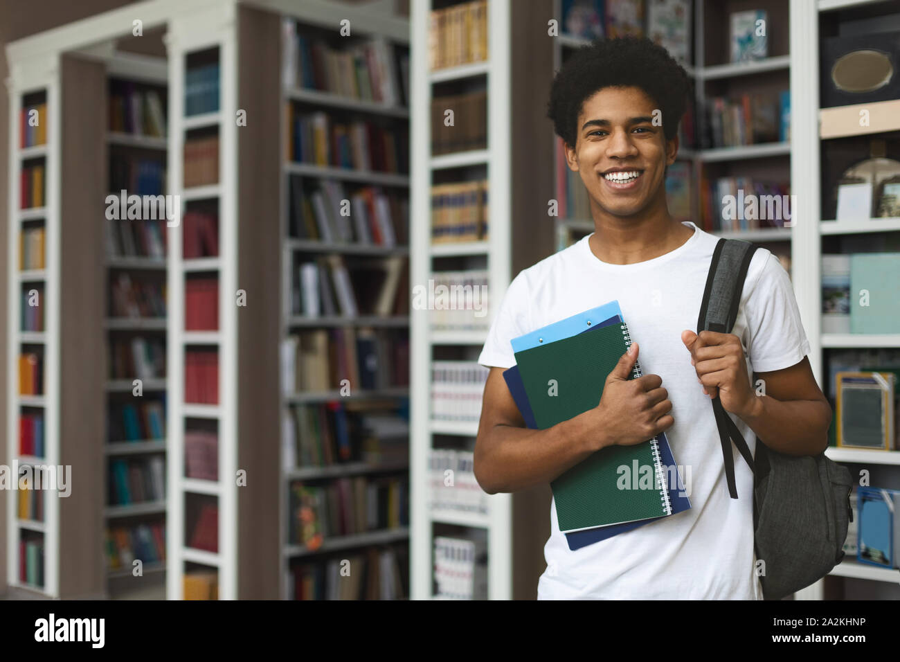 Handsome afro student posing on bookshelves background Stock Photo