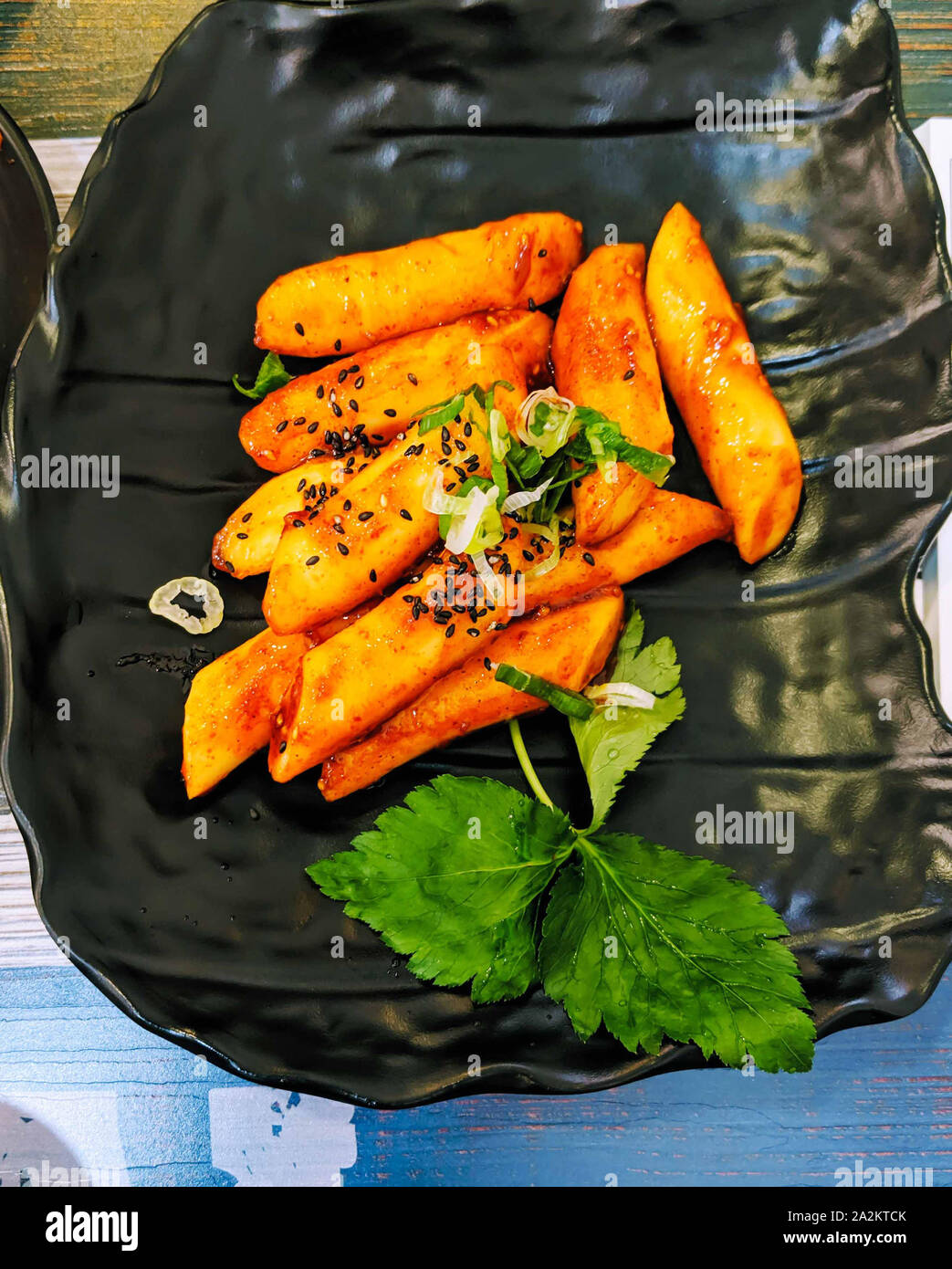 Korean penne pasta in tomato sauce with chicken, tomatoes decorated with parsley and sessame seeds on a wooden table Stock Photo