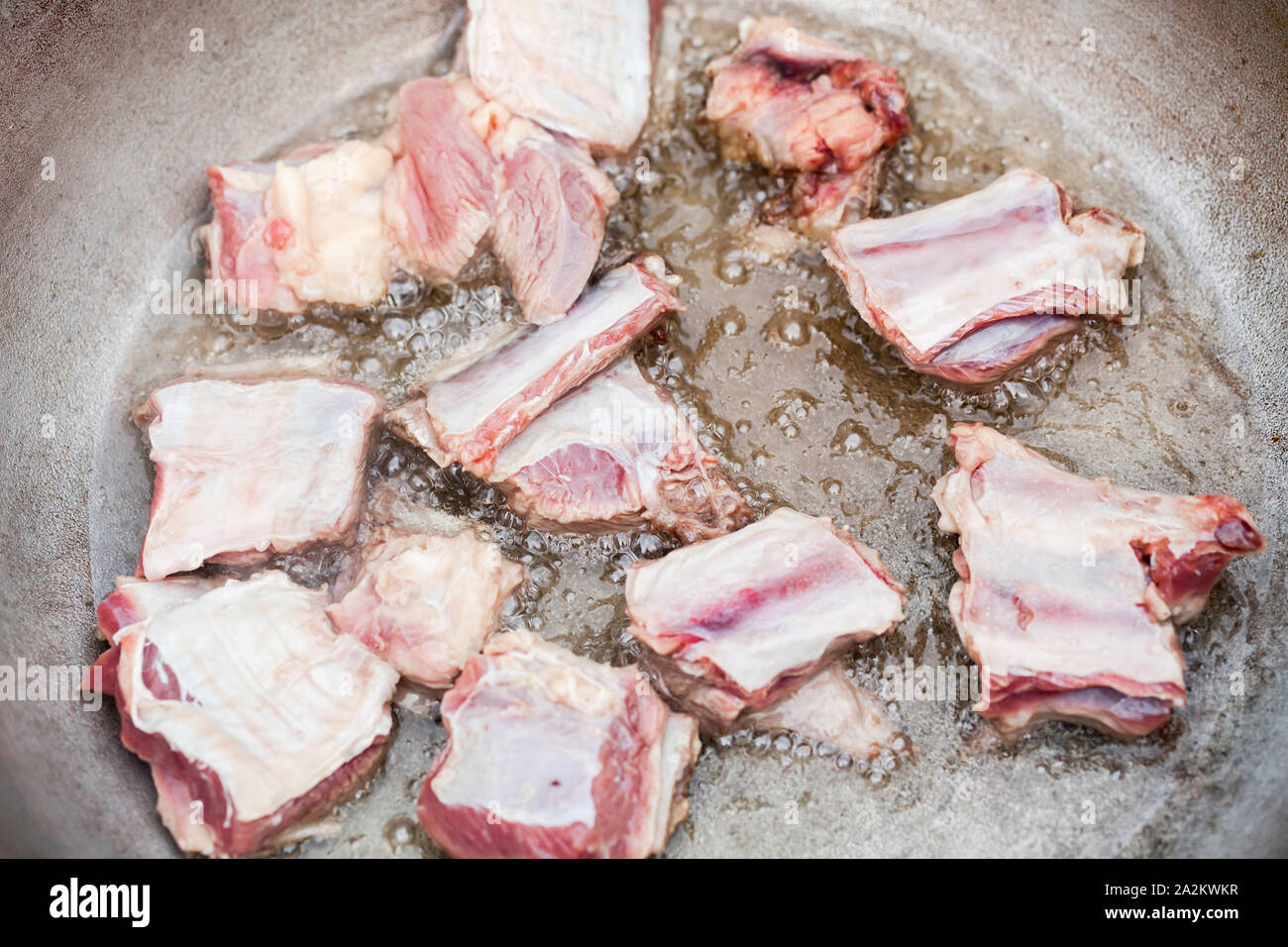 Beef pieces on bones stew in a cauldron with boiling oil. Top view
