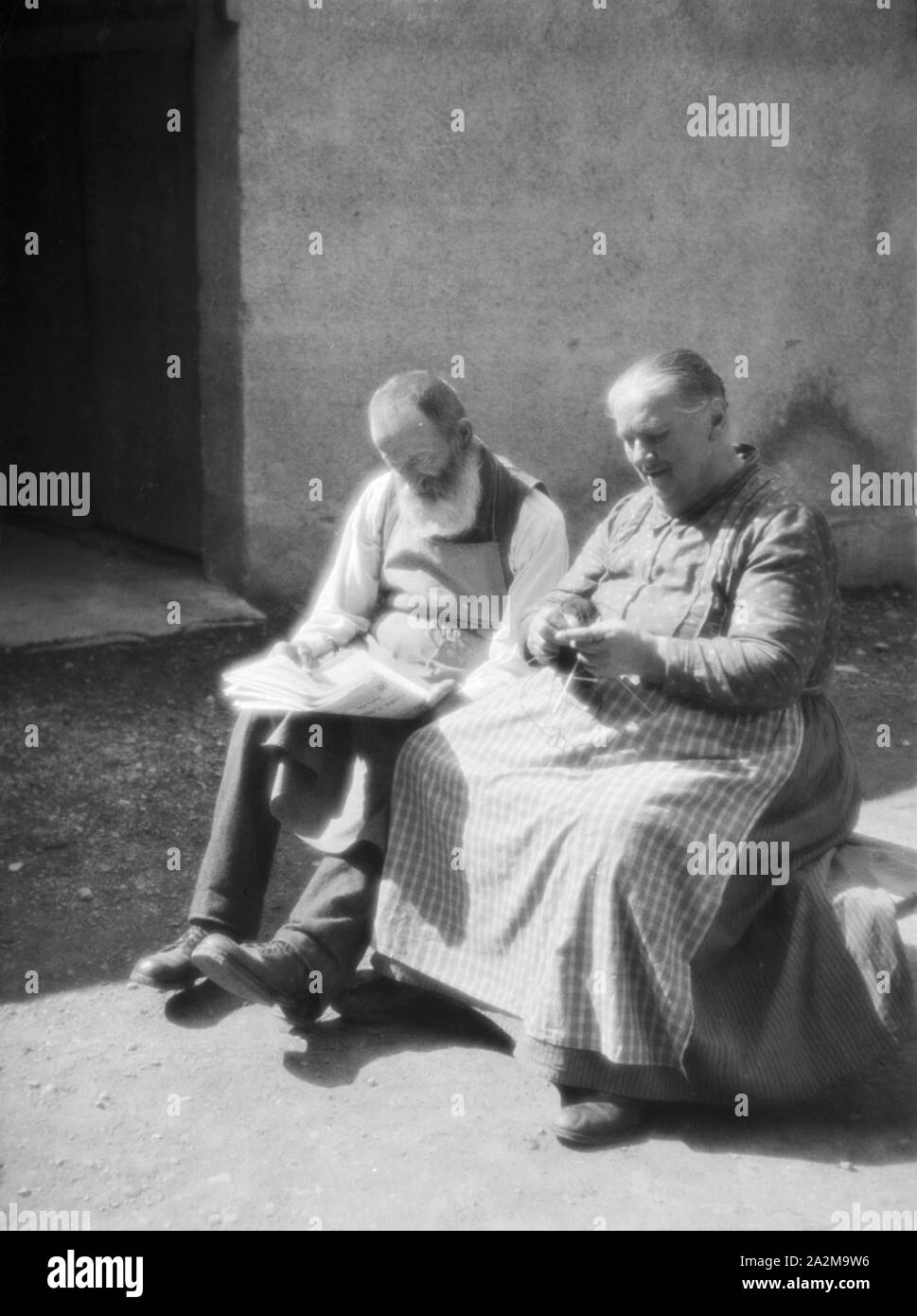 Ein altes Ehepaar sitzt im Hof in der Sonne, Deutschland 1930er Jahre. An old couple sitting in the sun in a courtyard, Germany 1930s. Stock Photo