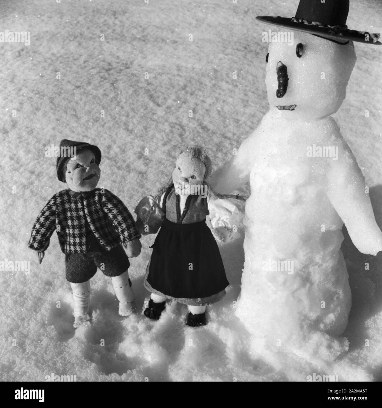 Zwei Puppen neben einem Schneemann, Deutschland 1930er Jahre. Two dolls with a snowman, Germany 1930s. Stock Photo