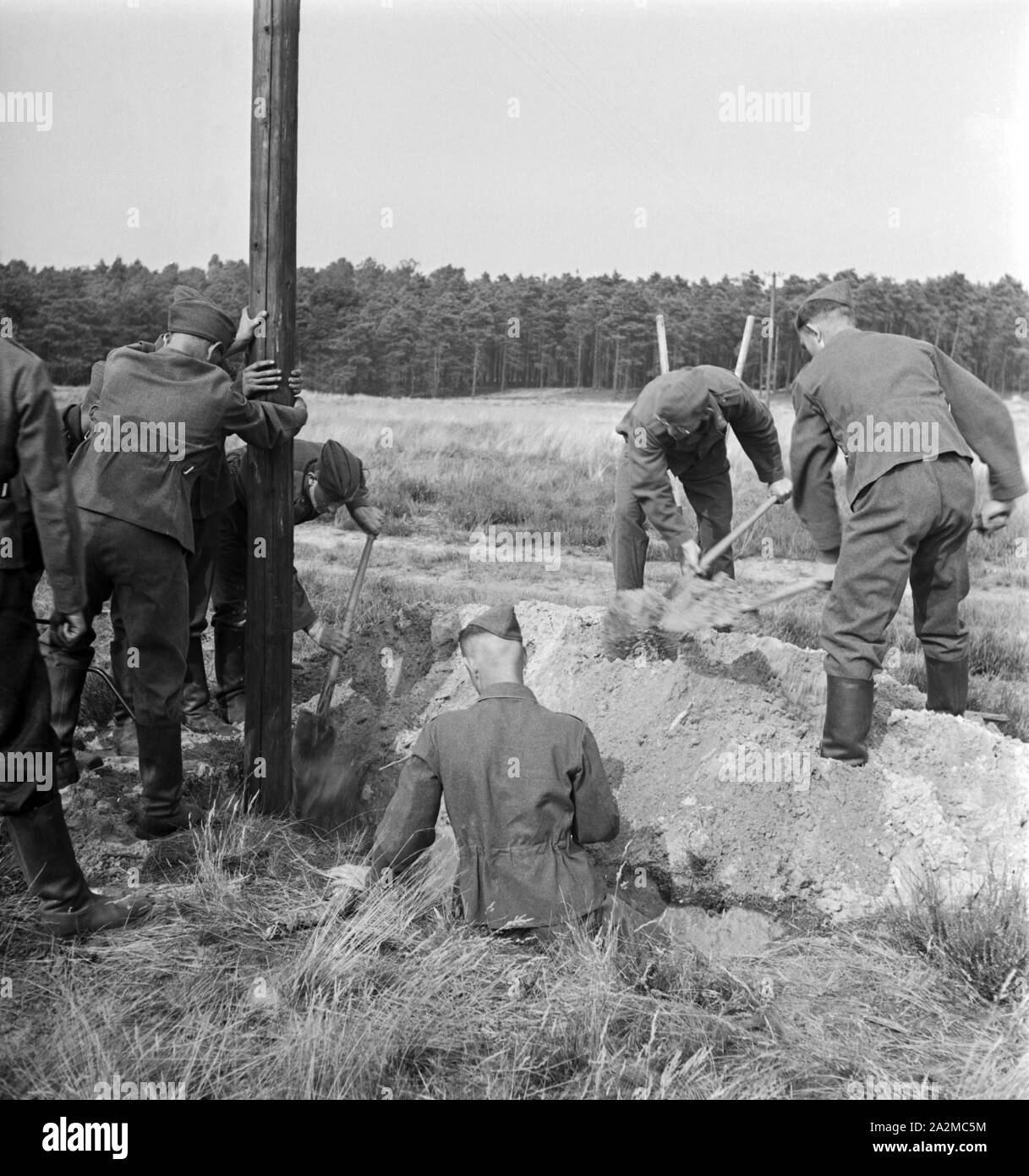 Original-Bildunterschrift: Ein Telegrafenbauzug bei der Arbeit - Masten werden im Gelände aufgstellt, Deutschland 1940er Jahre. A consruction group at work - telegraph masts are installed. Stock Photo