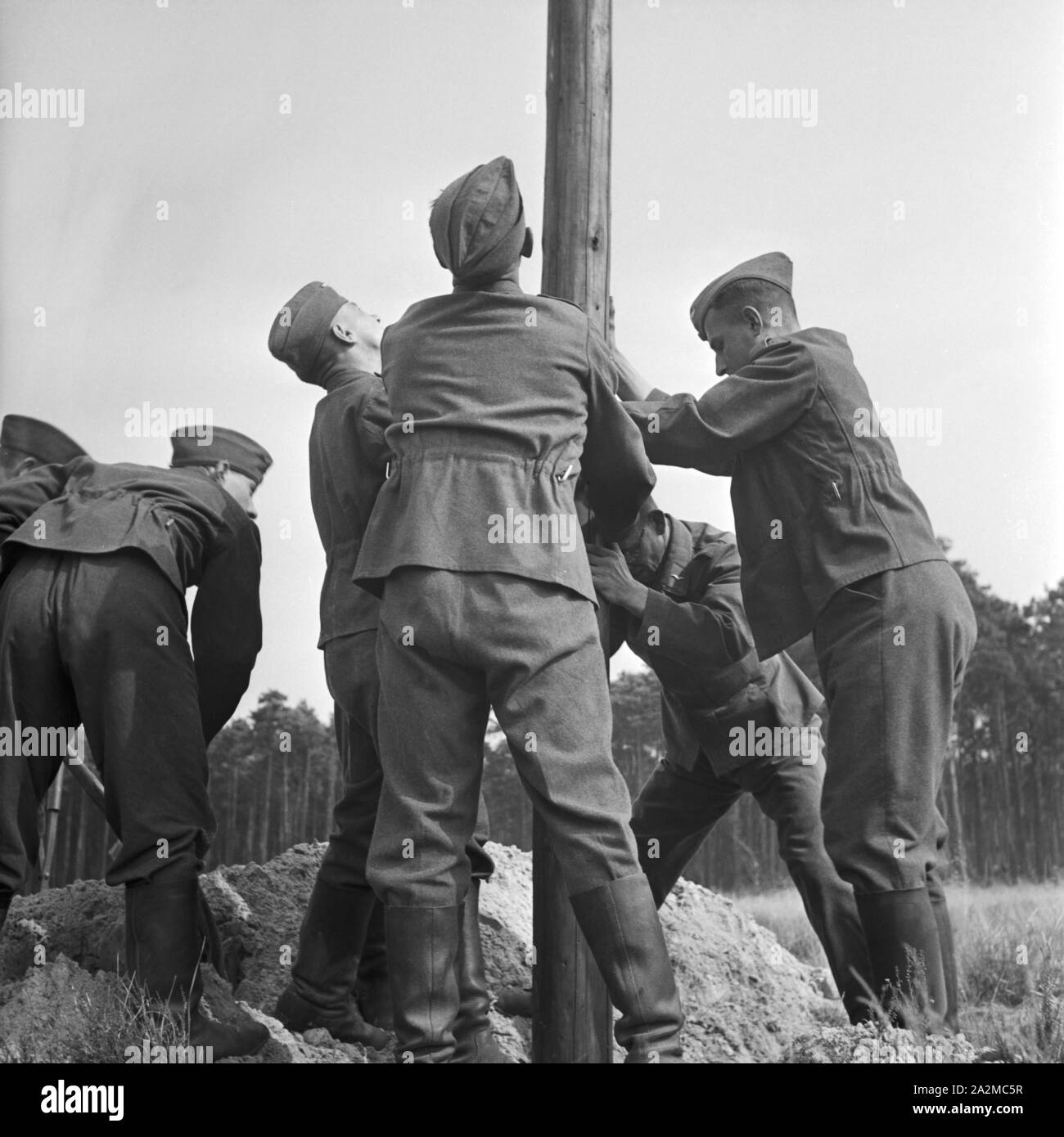 Original-Bildunterschrift: Ein Telegrafenbauzug bei der Arbeit - Masten werden im Gelände aufgstellt, Deutschland 1940er Jahre. A consruction group at work - telegraph masts are installed. Stock Photo