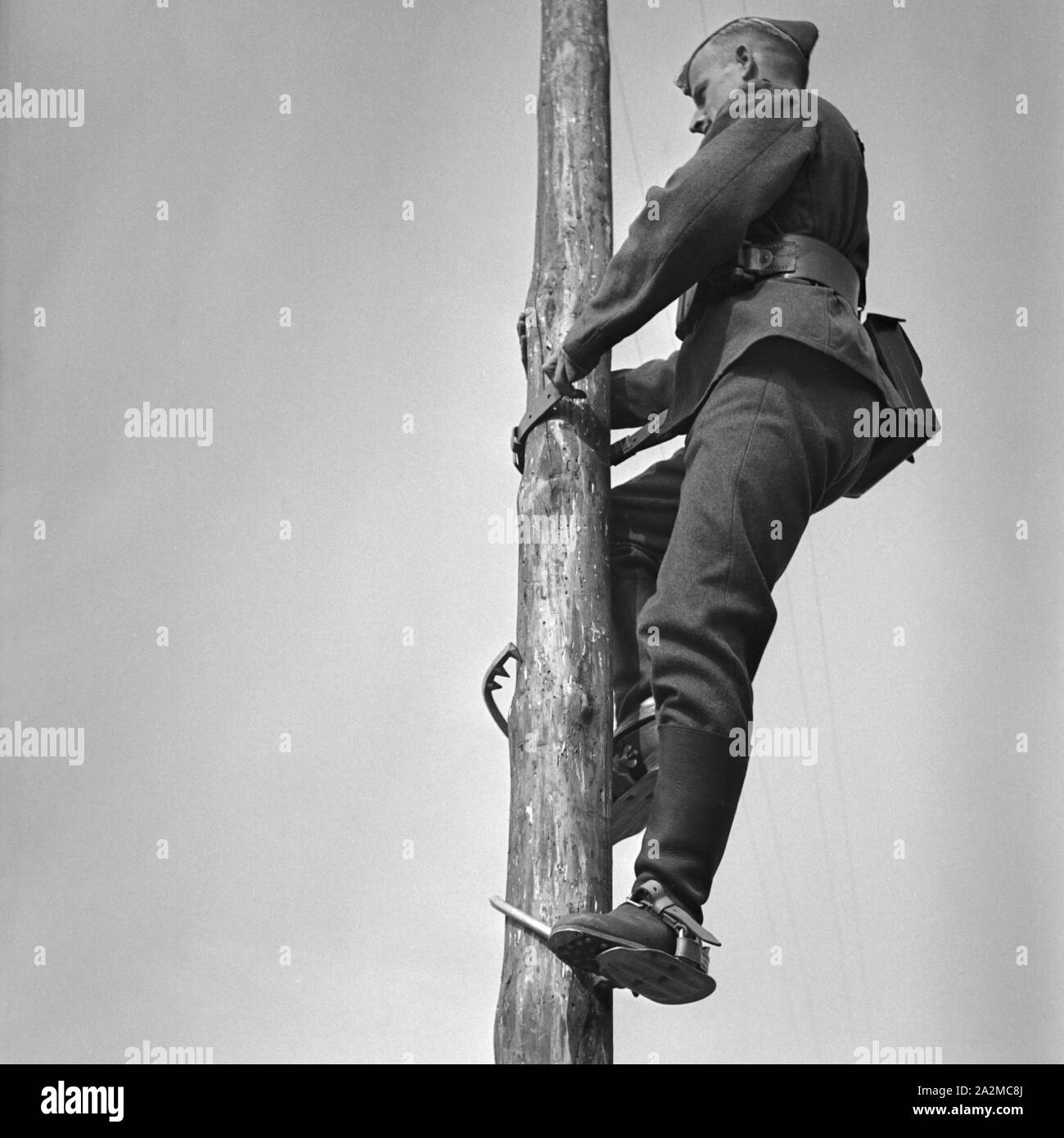 Original-Bildunterschrift: Soldat eines Telegrafenbauzugs besteigt einen Mast mit Steigeisen, Deutschland 1940er Jahre. Soldier of a pioneer construction climbing up a telegraph mast, Germany 1940s. Stock Photo