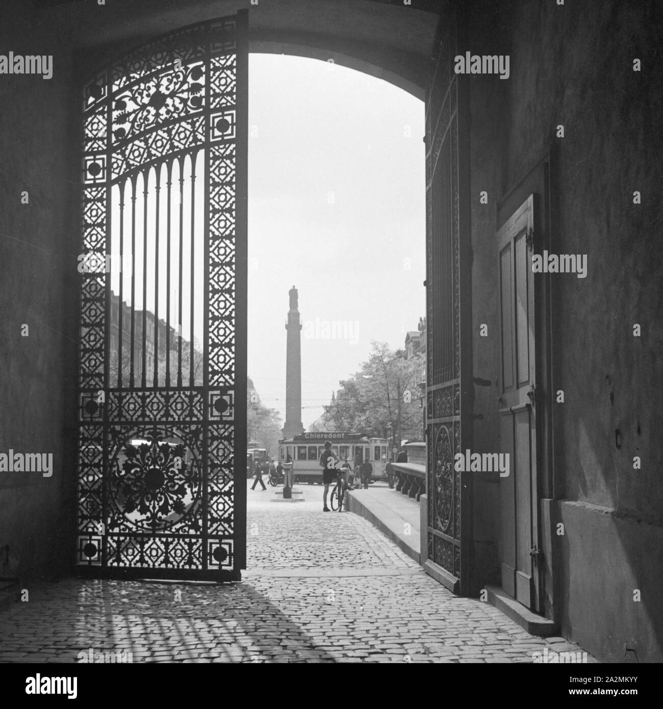 Blick durch ein schmiedeeiserne Tor auf das Stadtleben in Darmstadt, Deutschland 1930er Jahre. View through a wrought iron gate to the city life at Darmstadt, Germany 1930s. Stock Photo