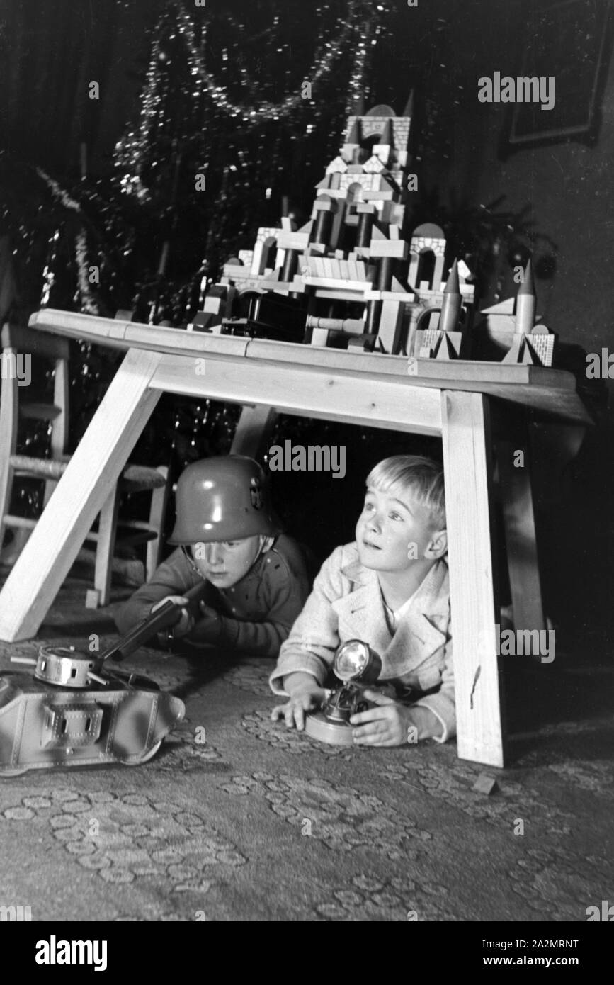 Two boys playing soldiers with a steel helmet and a toy rifle under the christmas tree, Germany 1930s Stock Photo