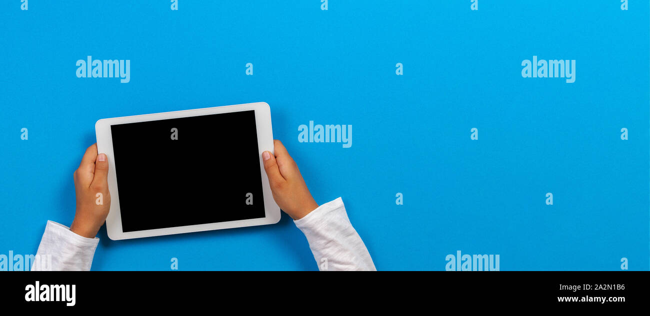 Kid hand holding white tablet computer on light blue background Stock Photo