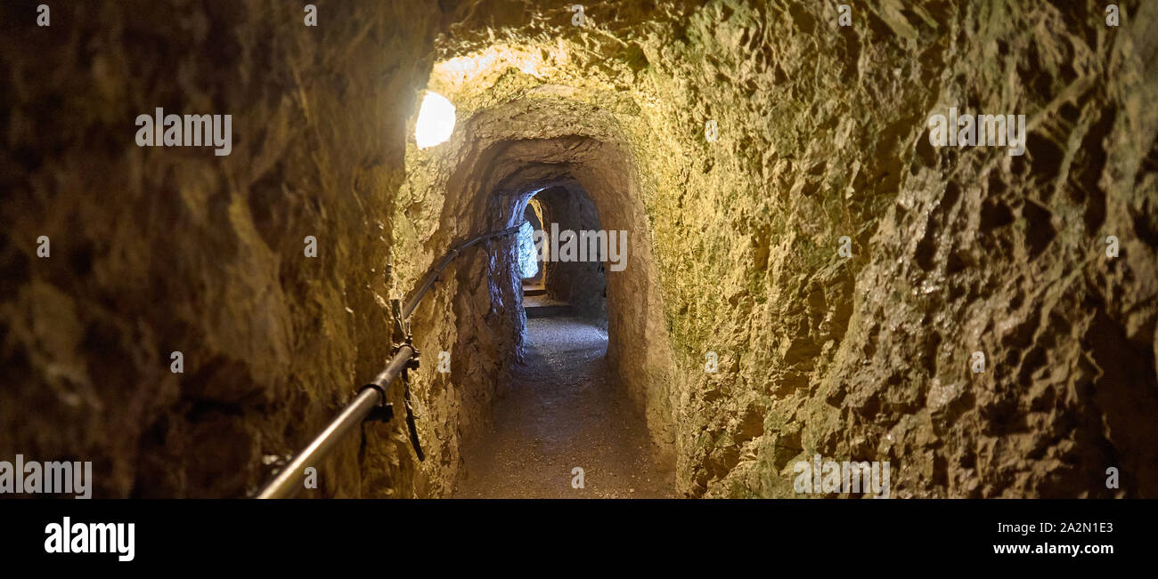 View through a narrow tunnel in the mountains made of limestone with an electric lamp on the ceiling. Stock Photo