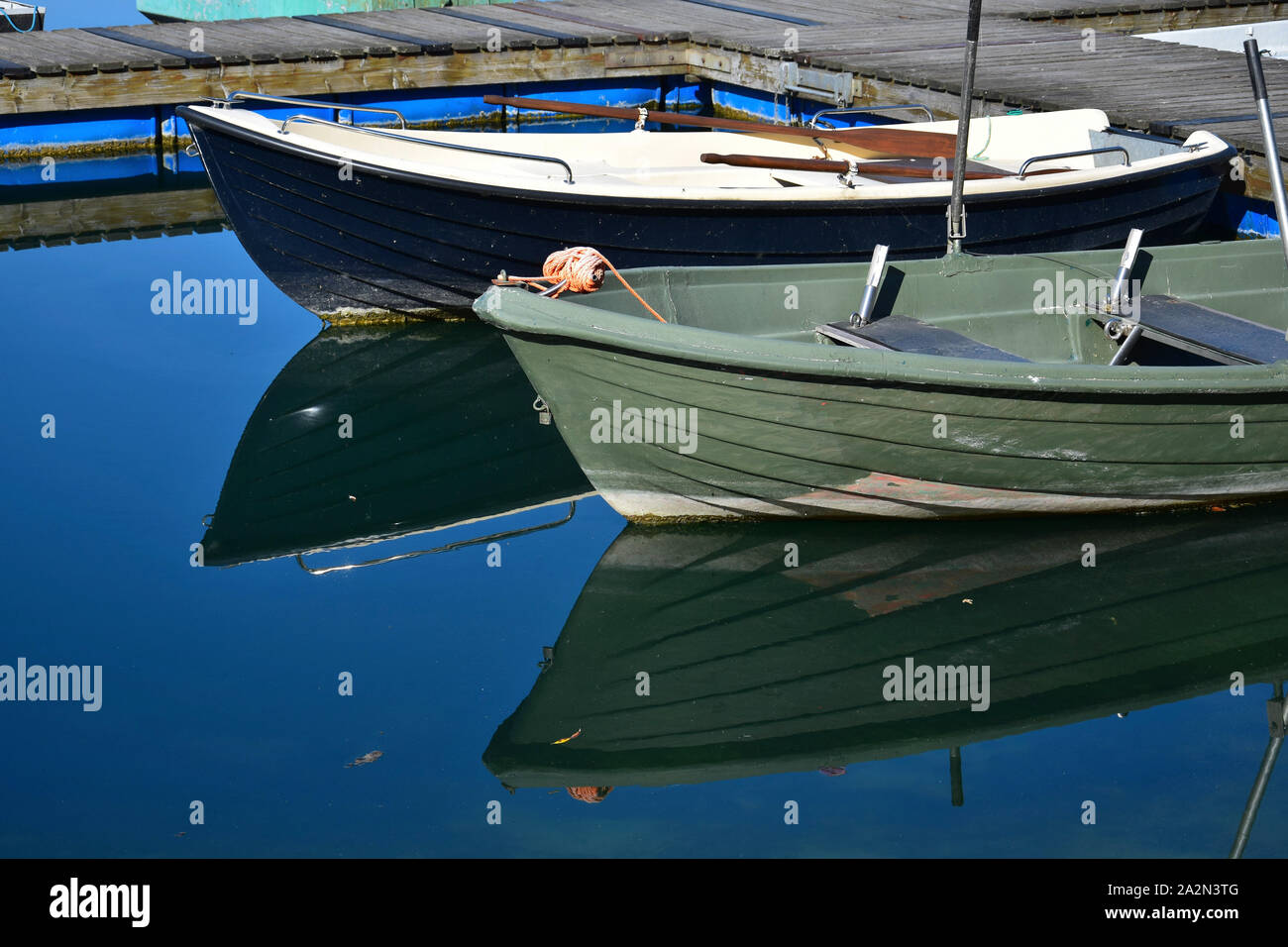 Two angler boats in a lake, one green and one black, reflecting in the water. Stock Photo