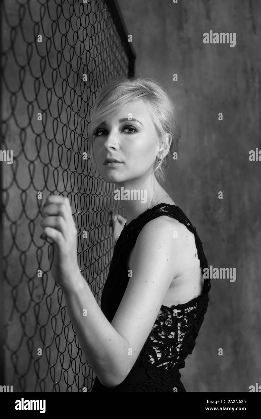 Blond beautiful woman standing at the metal mesh and holfing it Stock ...