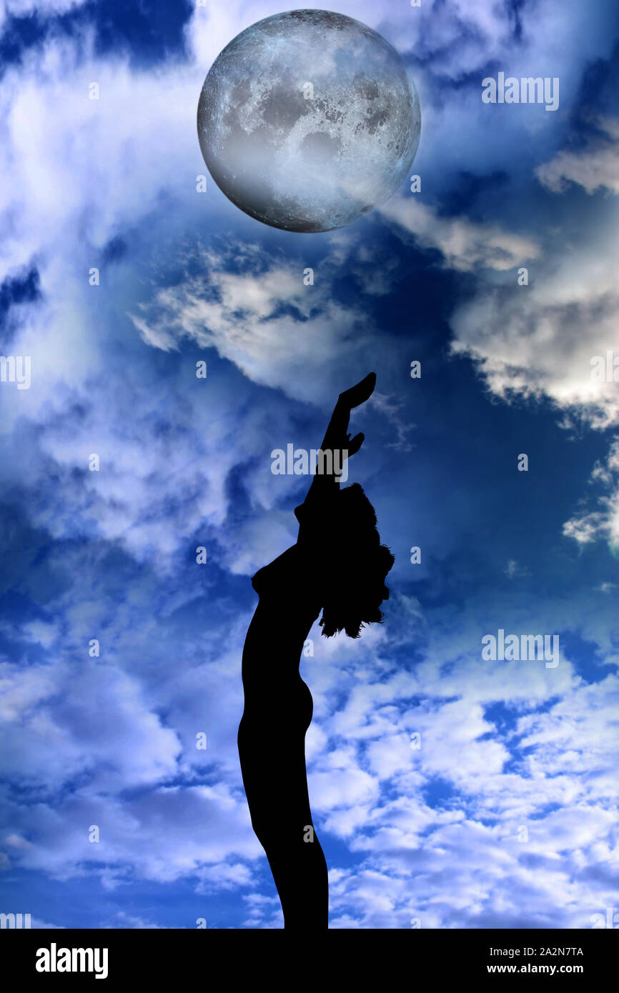 attractive silhouetted nude woman holding her hands up to the sky giving gratitude to the heavens in a yoga pose with a cloudy background Stock Photo