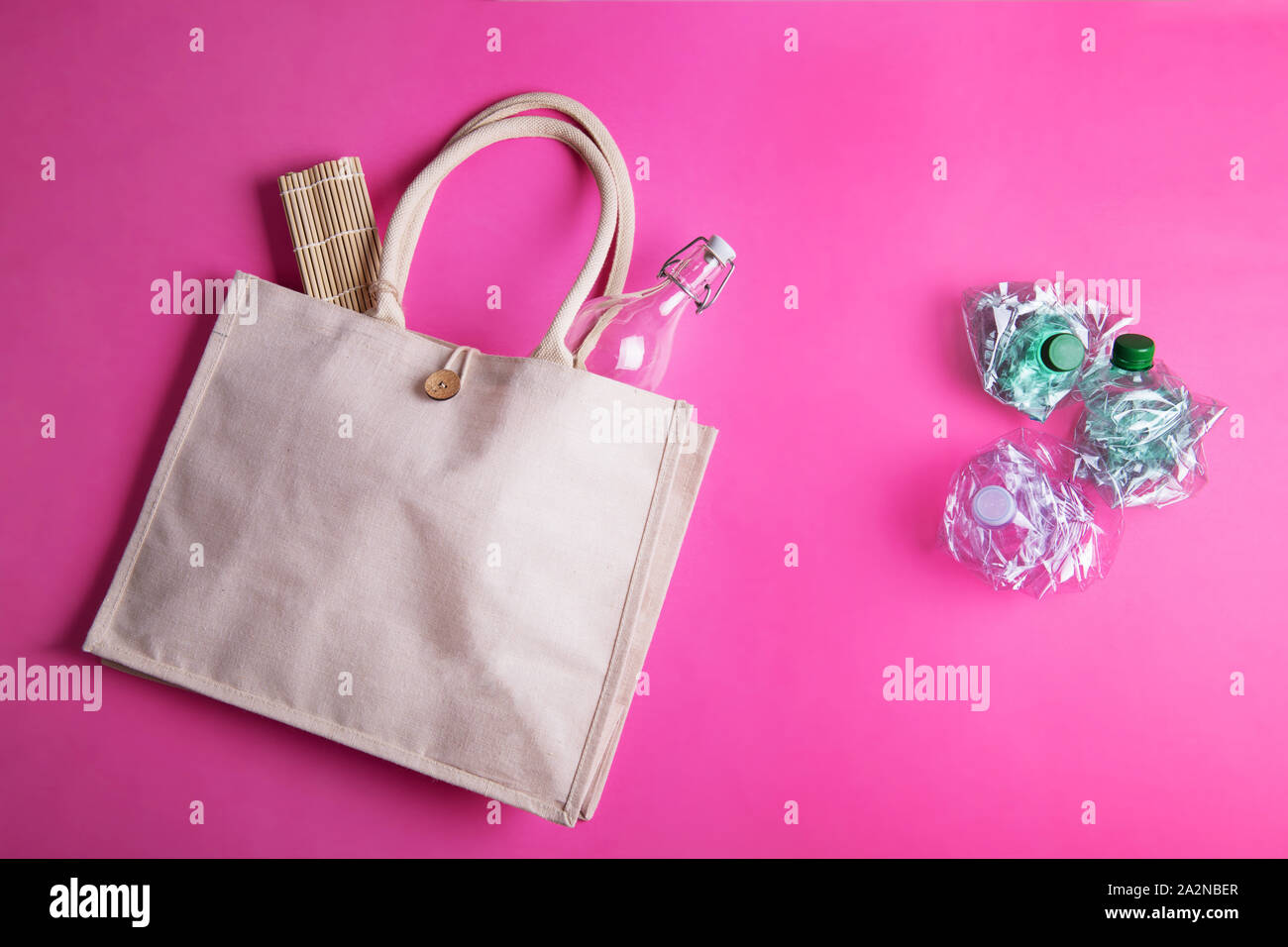 Reusable eco Cotton bag with a glass bottle and three crumpled plastic bottles on a bright pink