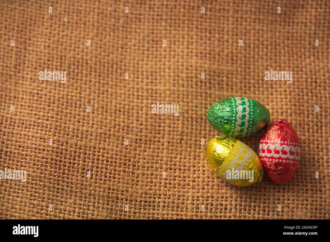 A decorative background for Easter with brightly colored eggs on a brown sackcloth and space to add texts or graphics. Copy Space Stock Photo