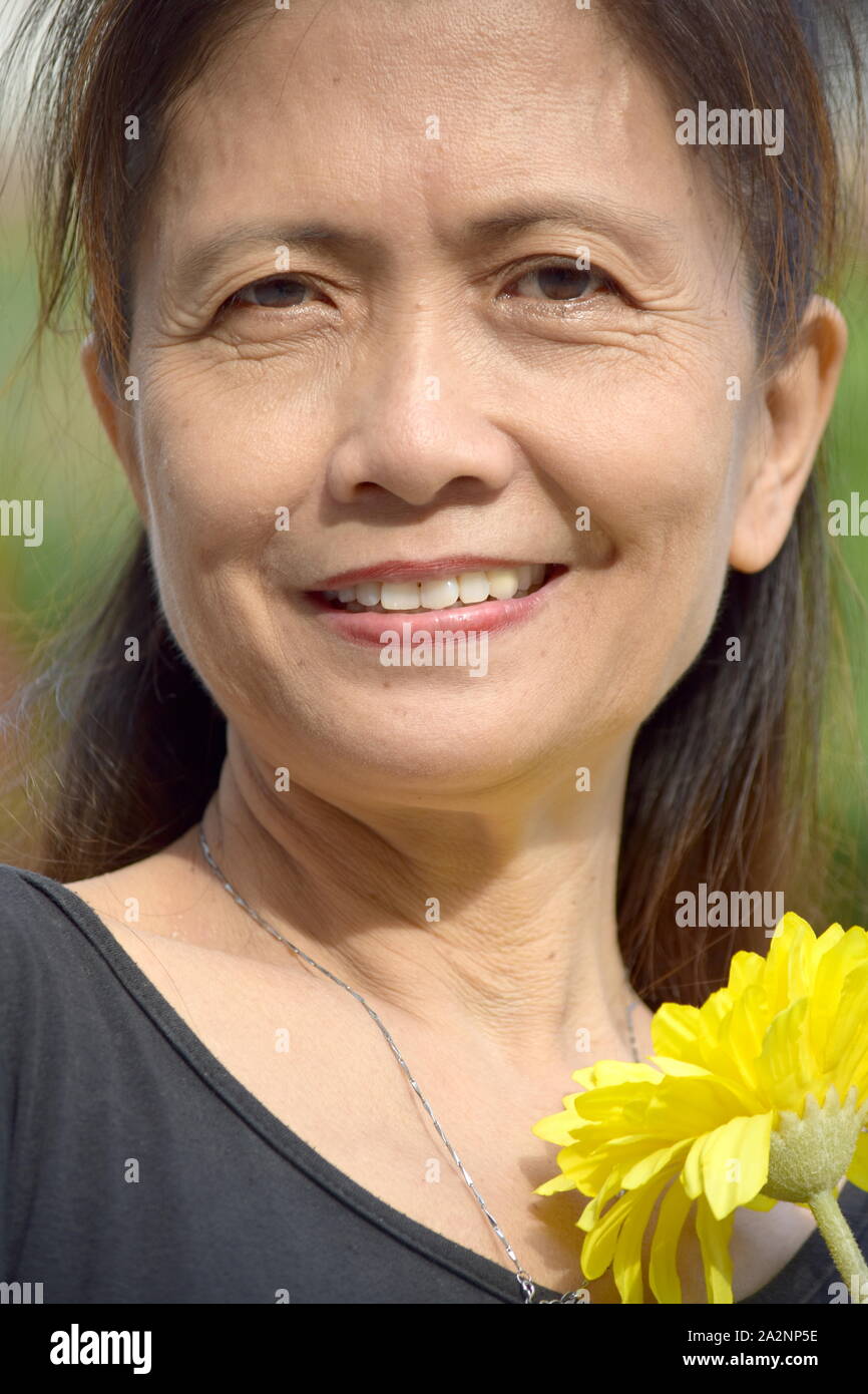 Retired Female Senior Smiling With A Daisy Stock Photo