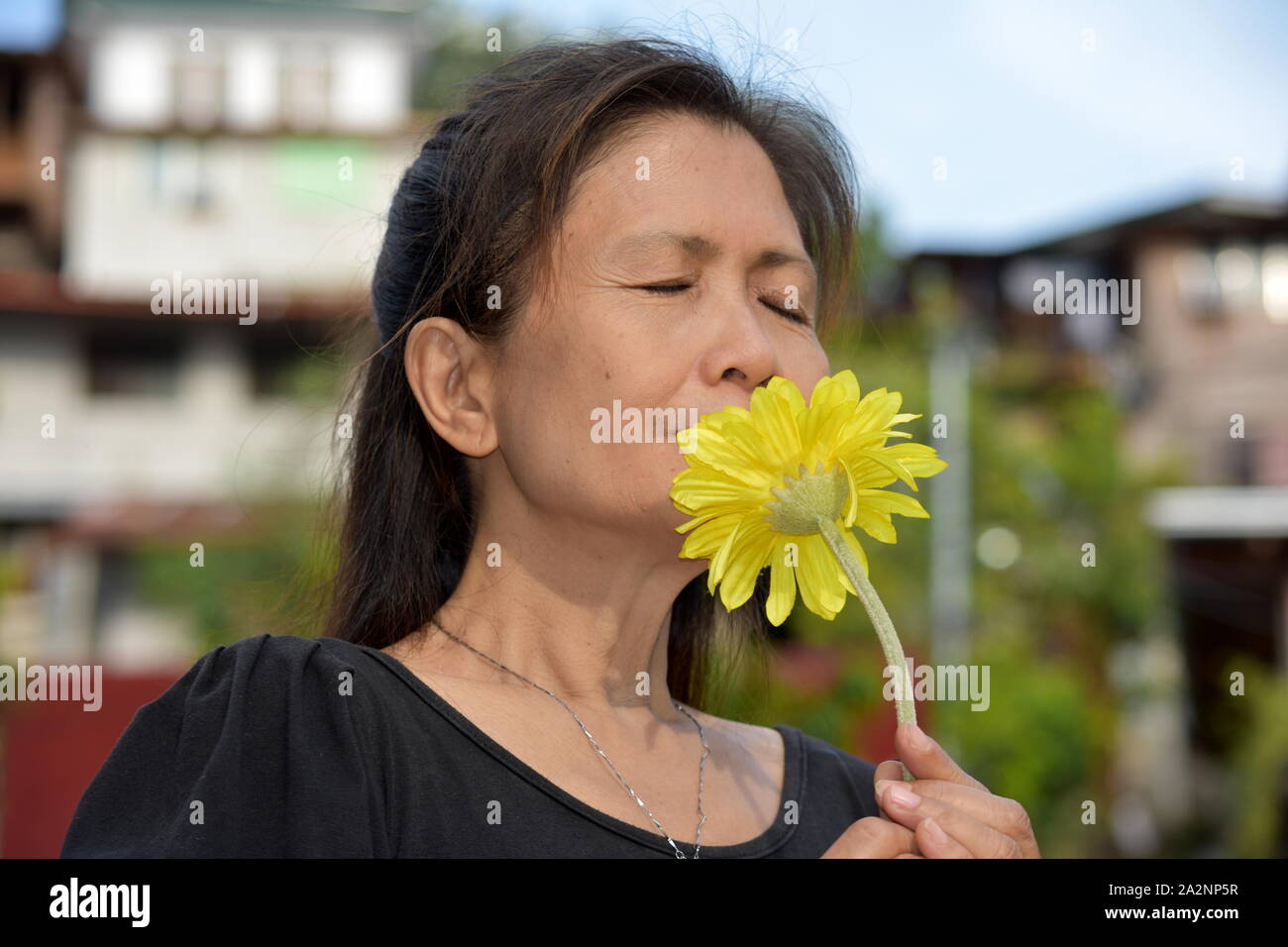 Filipina Female Senior And Poverty Smelling Flowers Stock Photo